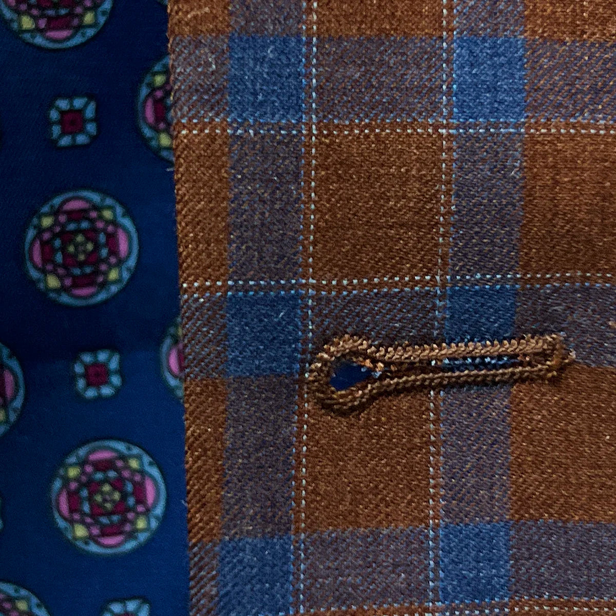 Macro view of hand-finished buttonhole stitching showing precision craftsmanship and red accent threading against check pattern
