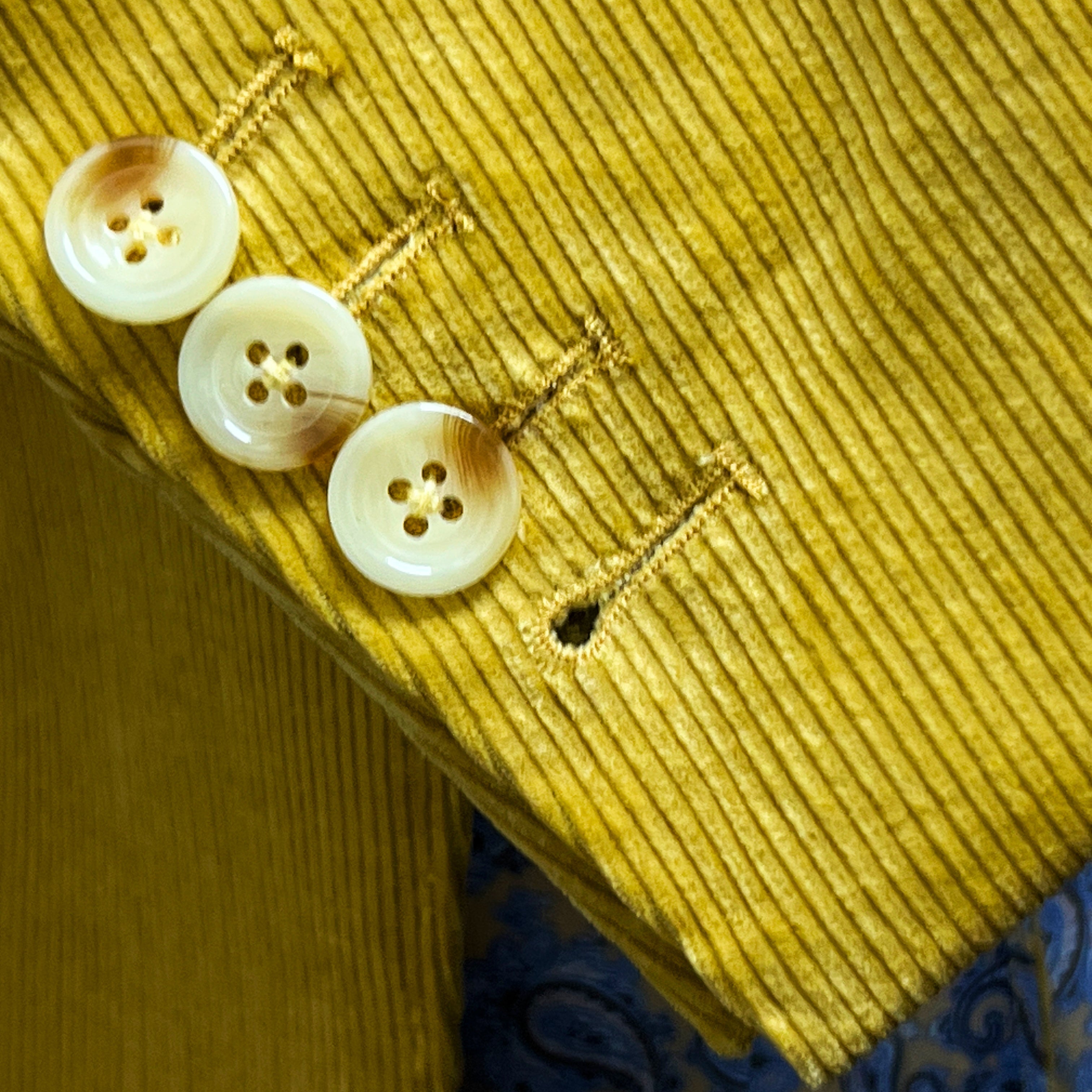 Sport coat sleeve cuff showing functional buttonholes with hand-finished stitching on warm mustard yellow corduroy fabric