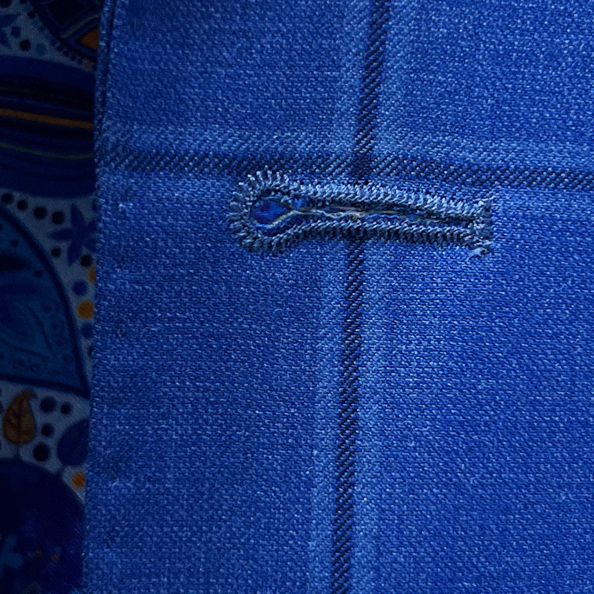 Detailed macro shot of hand-finished buttonhole stitching on royal blue windowpane suit with dark blue contrast thread